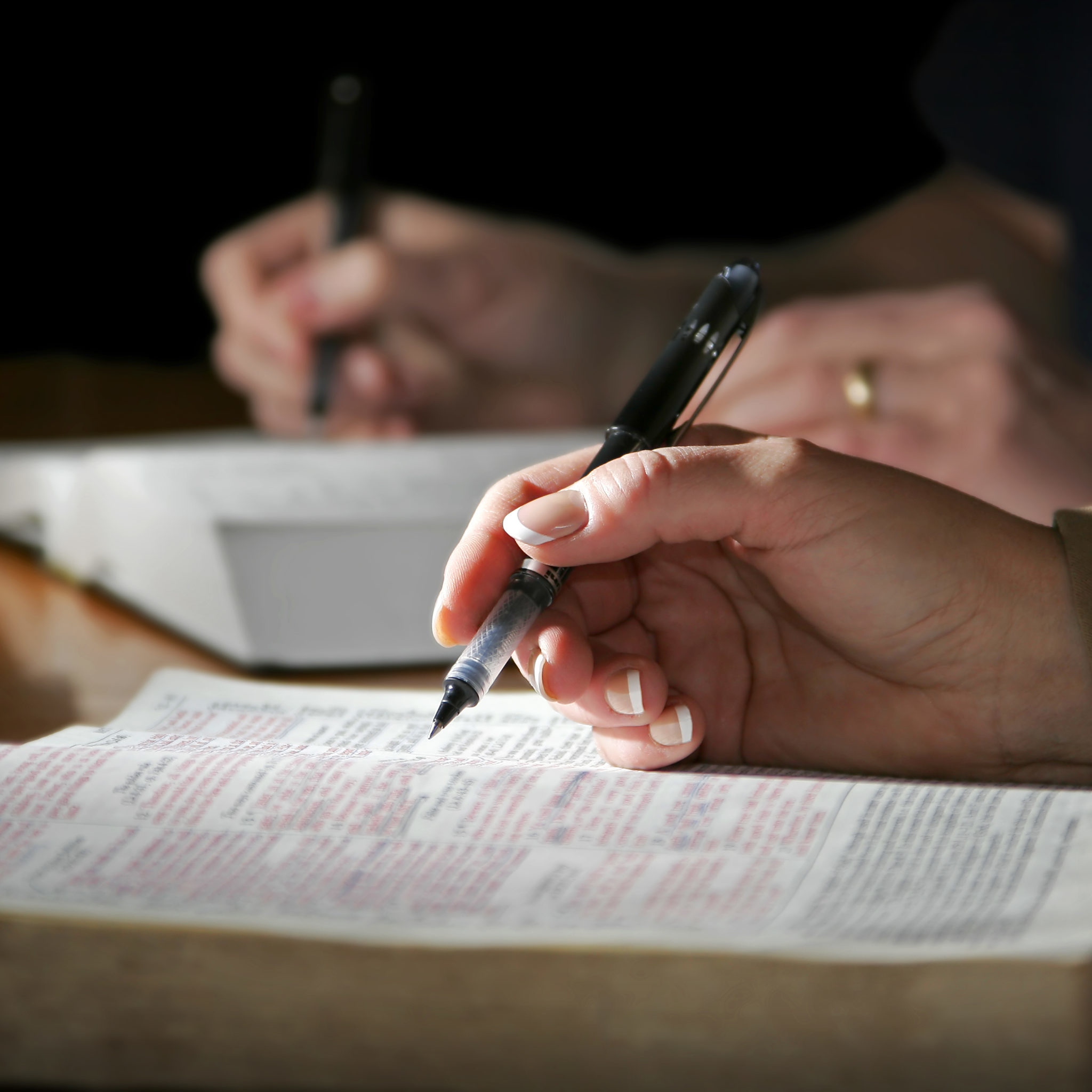The hands of a couple are highlighted as they study the Holy Bible together - focus point on the woman's foreground hand.